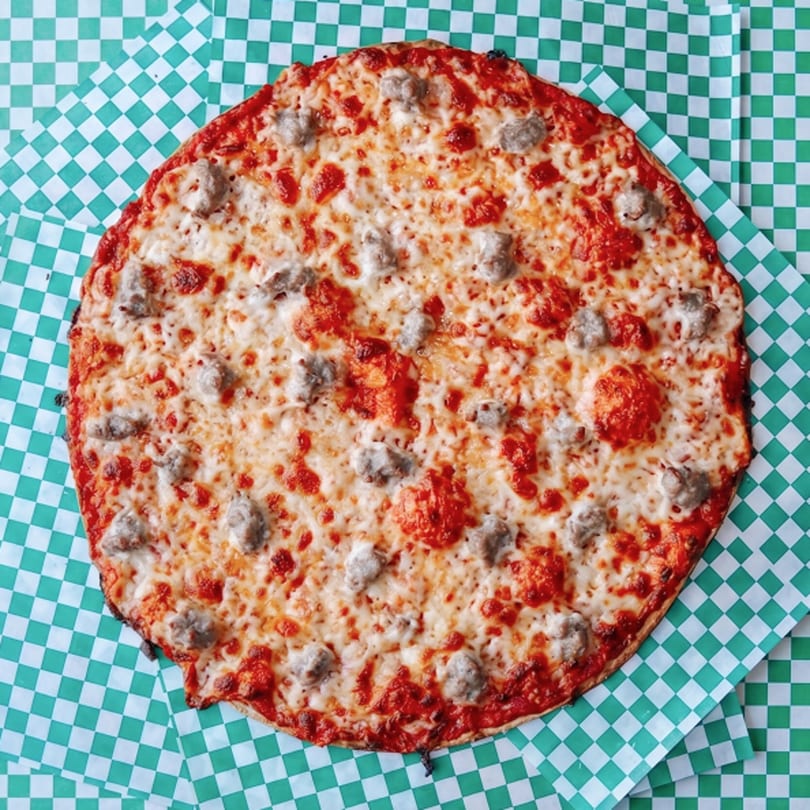 A round sausage pizza with melted cheese and red sauce on green and white checkered paper.