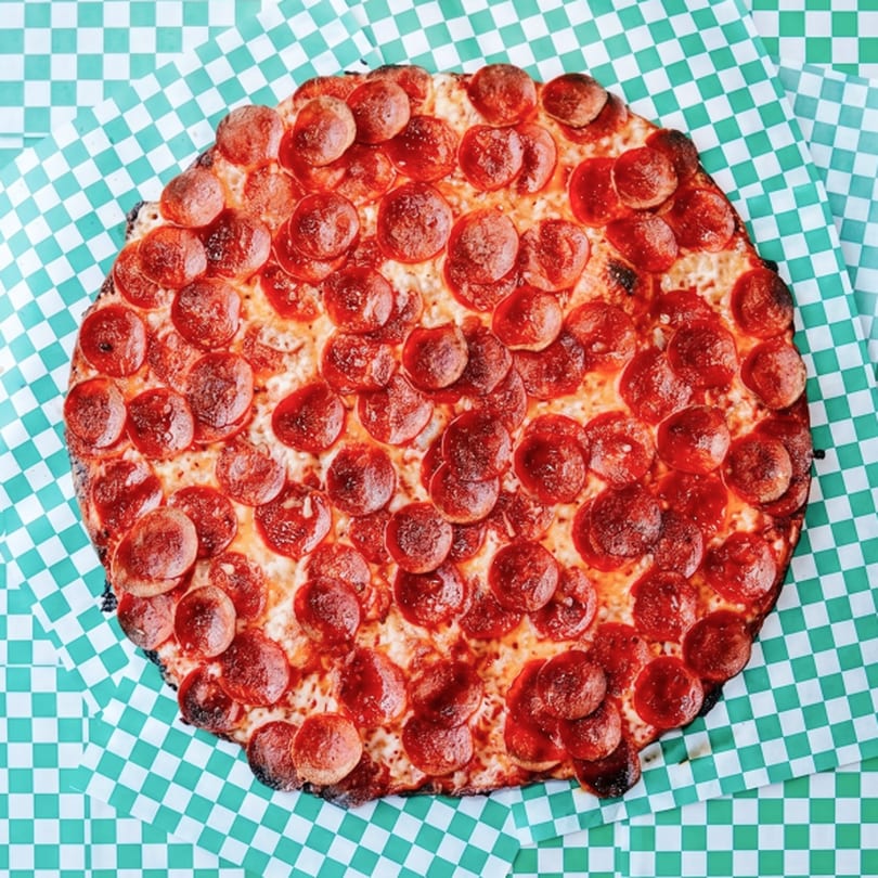 A round pepperoni pizza with a crispy crust sits on green and white checkered paper.